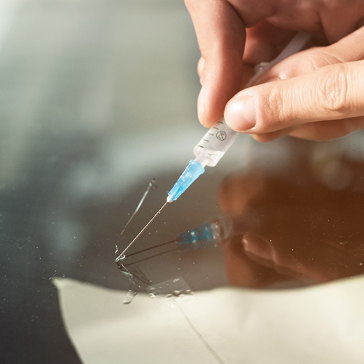 Close-up of a professional windshield repairman fills a crack in the glass with a special polymer through a syringe. Elimination of cracks and chips on windshields