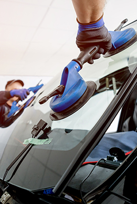 Automobile special workers replacing windscreen or windshield of a car in auto service station garage.
