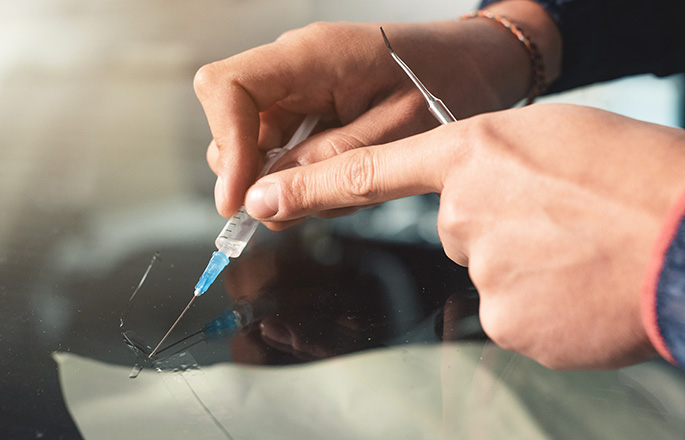 Close-up of a hands of professional windshield repairman fills a crack in the glass with a special polymer through a syringe. Elimination of cracks and chips on windshields