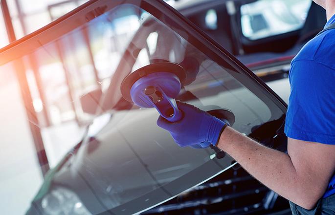 Automobile special workers replacing windscreen or windshield of a car in auto service station garage.